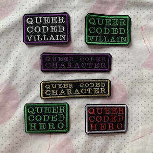 May include: Six embroidered patches with black fabric and colourful text. The patches read "Queer Coded Villain", "Queer Coded Villain", "Queer Coded Character", "Queer Coded Character", "Queer Coded Hero", and "Queer Coded Hero".