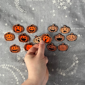 Op de afbeelding: Een verzameling van 12 oranje en zwarte vilt-pompoenpatches. De patches zijn in verschillende maten en vormen, sommige met een eenvoudig pompoengezicht en andere met een meer gedetailleerd ontwerp.