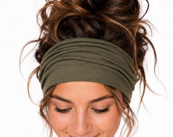 May include: A wide, olive green fabric headband with a gathered, ruched texture. The headband is positioned horizontally across the forehead, featuring a soft, matte finish and a flexible, stretchy construction that sits snugly against the hair.