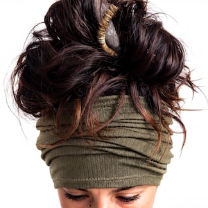 A close-up view of a person's head, with their hair styled in a messy bun and wearing a green headband.