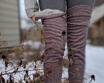 Könnte beinhalten: Ein Paar heather-pflaumenfarbene, oberschenkelhohe Stulpen aus geripptem, strukturiertem Strickstoff. Die Stulpen reichen von der Mitte des Oberschenkels abwärts und zeigen am oberen Rand ein weiches, hellgraues, fleeceartiges Innenfutter.