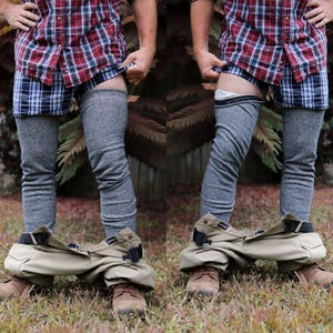 May include: A person wearing a red and black checked shirt, grey leg warmers, and khaki trousers. The trousers are pulled down to reveal the leg warmers.