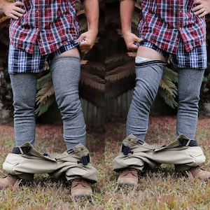 May include: A red and blue plaid button-down shirt worn over blue plaid boxers and grey thermal leggings, paired with tan trousers pulled down to the ankles and brown leather boots. The outfit includes a black belt with a plastic buckle.