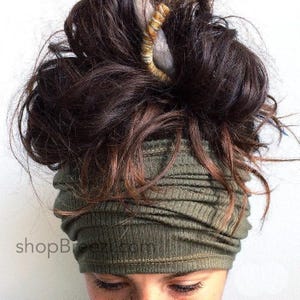 Peut inclure: Un bandeau en tissu côtelé vert olive porté autour du front, présentant une surface texturée avec des coutures horizontales. Le texte shopbreezi.com est visible dans le coin inférieur gauche. Des cheveux bruns sont coiffés en chignon.