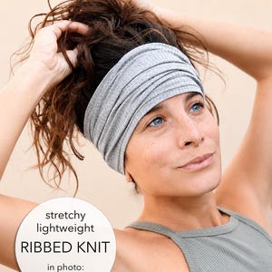 A woman with brown hair is adjusting her gray headband, wearing a gray tank top.