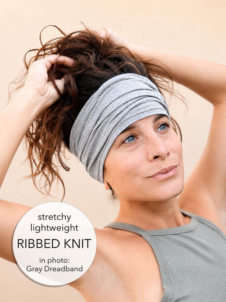 A woman with brown hair is adjusting her gray headband, wearing a gray tank top.