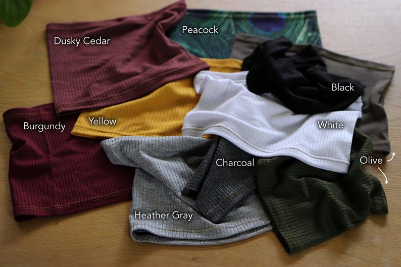 a variety of colorful clothing items, including a red scarf, a black scarf, a white shirt, a maroon scarf, a yellow scarf, a black scarf, a white shirt, a gray scarf, a charcoal scarf, a black scarf, a white shirt, a gray scarf, a black scarf, a white shirt, an olive scarf, and a gray scarf, all laid out on a wooden surface.