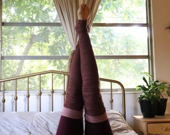May include: A pair of long, maroon-colored leg warmers featuring a textured, ruched fabric design. The leg warmers extend from the upper thigh down to the ankle, showcasing a lighter pink horizontal band detail near the lower section of the garment.