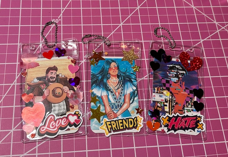 Pode incluir: Tr&ecirc;s porta-crach&aacute;s de pl&aacute;stico transparente com inser&ccedil;&otilde;es decorativas. Um tem uma imagem de cowboy com a palavra "Love", outro uma mulher com a palavra "Friends" e o &uacute;ltimo uma paisagem urbana com a palavra "Hate". Cada um tem enfeites de cora&ccedil;&atilde;o e estrela.