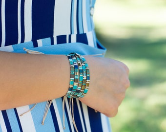 May include: A stack of turquoise, gold, and white beaded bracelets on a person's wrist.