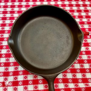 May include: A round black cast iron skillet with a smooth interior surface and two side pouring spouts. The handle features the embossed number 10. The pan has a dark, seasoned finish and a sturdy construction with a long handle for easy gripping.