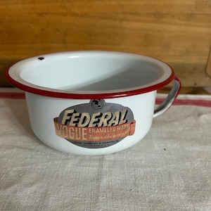 May include: White enamelware bowl with a red rim and handle. The bowl features the text "FEDERAL VOGUE ENAMELED WARE" on a sticker. The bowl is a vintage item.