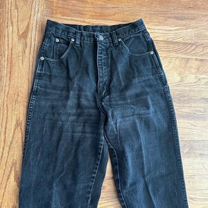 May include: Black denim jeans with a high waist and a button closure. The jeans have classic five-pocket styling and a straight leg. The fabric appears to be slightly faded, giving them a vintage look.