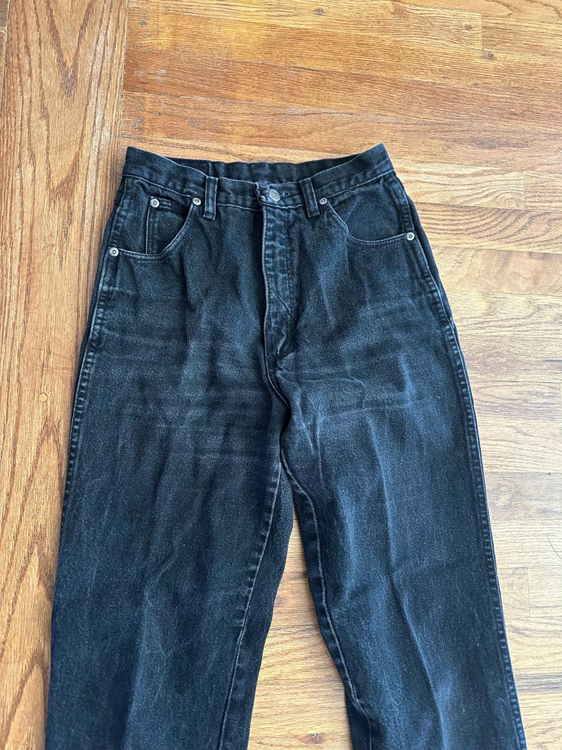 May include: Black denim jeans with a high waist and a button closure. The jeans have classic five-pocket styling and a straight leg. The fabric appears to be slightly faded, giving them a vintage look.