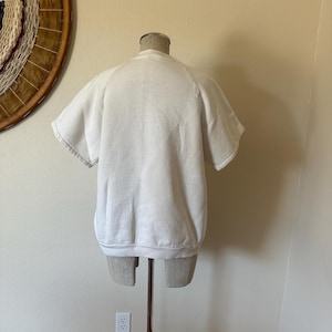 Op de afbeelding: Een witte sweatshirt met korte mouwen, getoond op een mannequin. De sweatshirt heeft een ronde hals en een relaxte pasvorm. De mouwen zijn kort en afgewerkt met een geribde boord. Het kledingstuk is gemaakt van zacht materiaal, waarschijnlijk katoen.