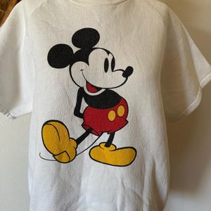 Op de afbeelding: Wit sweatshirt met korte mouwen met een grote Mickey Mouse-afbeelding. Het stripfiguur is afgebeeld in zwart, rood en geel, met een glimlach. De sweatshirt heeft een ronde hals en een relaxte pasvorm.