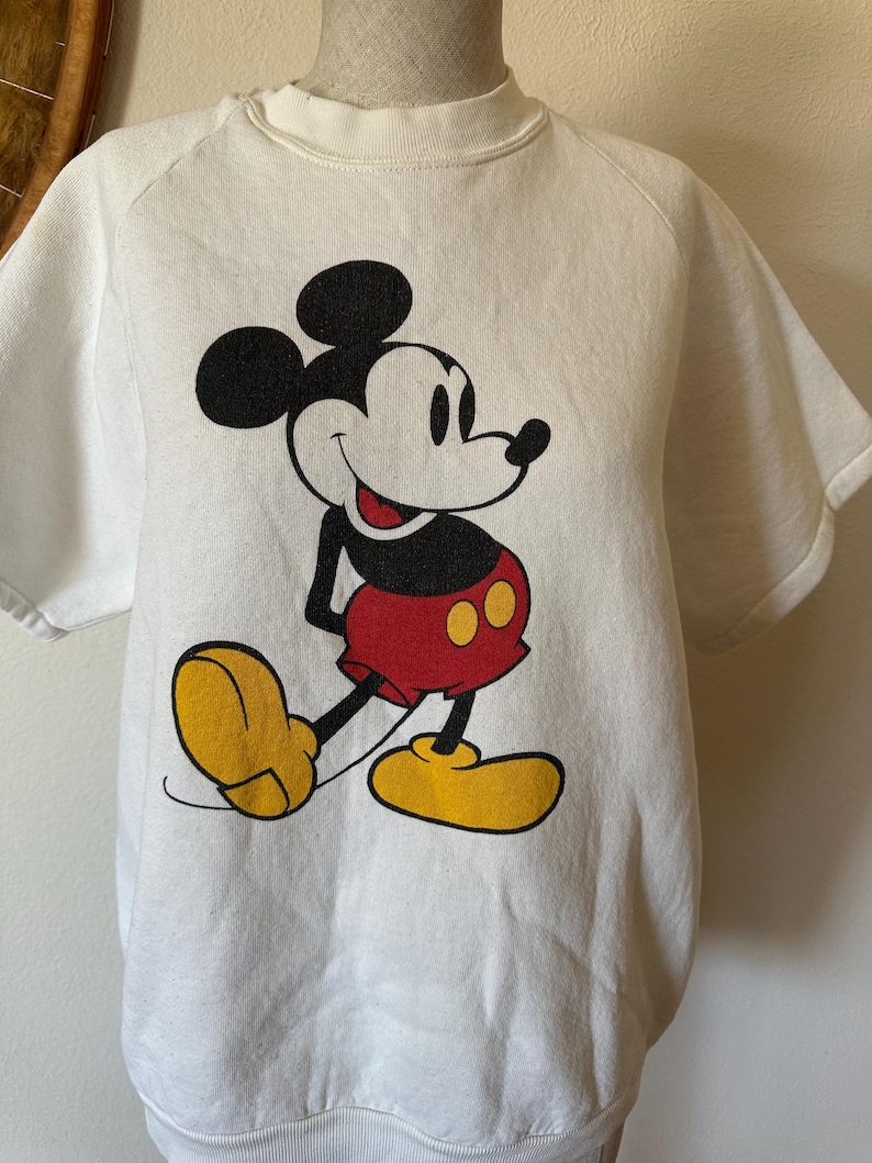 Op de afbeelding: Wit sweatshirt met korte mouwen met een grote Mickey Mouse-afbeelding. Het stripfiguur is afgebeeld in zwart, rood en geel, met een glimlach. De sweatshirt heeft een ronde hals en een relaxte pasvorm.
