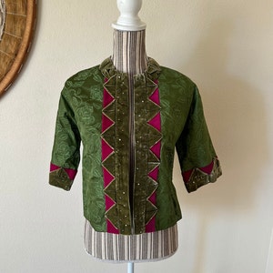 May include: Olive green jacket with a floral pattern, featuring a velvet collar and trim. The jacket has three-quarter sleeves and is accented with fuchsia panels and sparkling embellishments. The jacket is displayed on a mannequin.