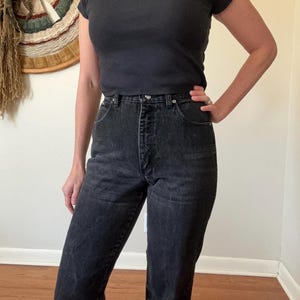 May include: Black short-sleeve ribbed top and high-waisted black jeans. The jeans have a classic five-pocket design and a button and zipper closure. The outfit is simple and casual, suitable for everyday wear.