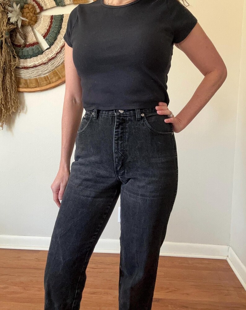 May include: Black short-sleeve ribbed top and high-waisted black jeans. The jeans have a classic five-pocket design and a button and zipper closure. The outfit is simple and casual, suitable for everyday wear.