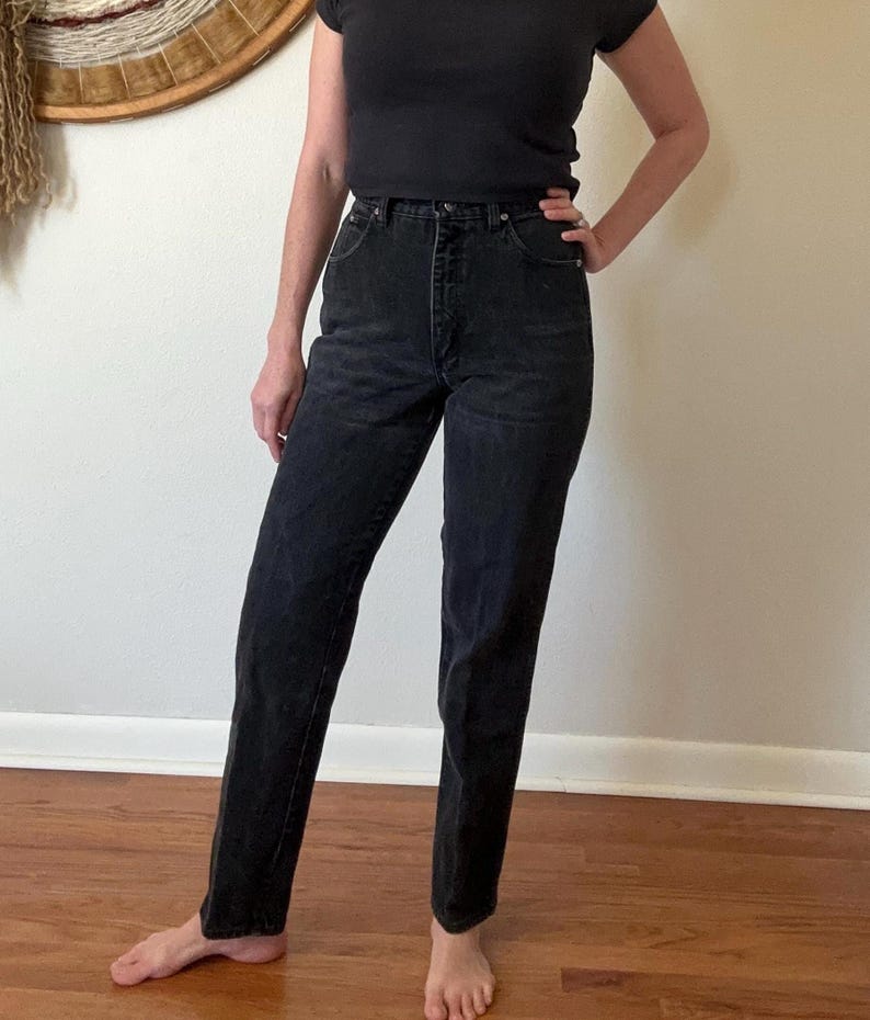 May include: Black denim jeans with a classic straight-leg fit. The jeans have a high waist and a button and zipper closure. The dark wash denim is a versatile wardrobe staple.