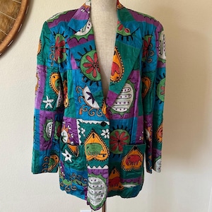 May include: A colorful blazer with a patchwork design. The jacket features a vibrant mix of teal, purple, green, and orange hues, adorned with various abstract shapes and patterns. The blazer has a classic collar, two front pockets, and a two-button closure.