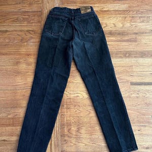 May include: Dark wash denim jeans with a classic five-pocket design. The jeans have a straight leg cut and a faded appearance, with a leather patch on the back waistband. The jeans are laid flat on a wooden surface.