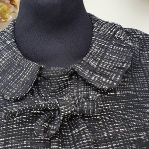 May include: A black and white patterned blouse with a Peter Pan collar and a bow tie detail at the neckline.