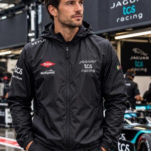 May include: A black hooded windbreaker jacket featuring the Jaguar TCS Racing logo on the chest, with additional sponsor branding including REFLO, Dow, Wolfspeed, and TCS Data Cloud printed in white on the sleeves and front panels.