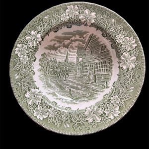 May include: A decorative plate with a green and white floral border. The central image depicts a black and white rural scene with a building marked "Post Office" and figures on a road. The plate has a scalloped edge.