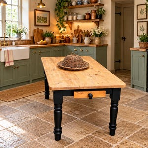 May include: A rectangular kitchen island with a natural light wood top and four black turned legs. The island features a single small drawer with a black knob on the front. A woven wicker dome-shaped food cover sits centred on the wooden surface.