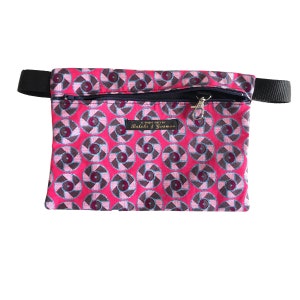 May include: A pink zippered pouch with a black strap and a repeating pattern of pink, brown, and blue circles. The pouch has a label that reads "A UNIQUE PIECE BY Buleki & Cosmos".