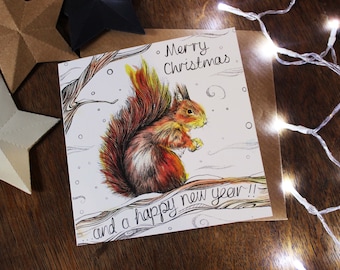 Pode incluir: Cartão de Natal com uma ilustração de um esquilo com cauda vermelha num cenário de neve. O cartão tem o texto "Merry Christmas and a happy new year !!". O cartão está numa superfície de madeira.