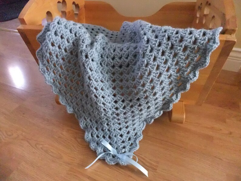 May include: A light blue crocheted baby blanket with a light blue ribbon tied at the bottom.