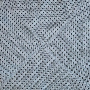 May include: A close-up of a gray crocheted blanket with a square pattern.