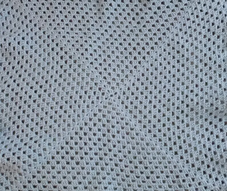 May include: A close-up of a gray crocheted blanket with a square pattern.