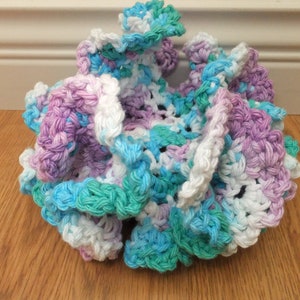 May include: A crocheted scrubby in shades of white, purple, blue, and green. The scrubby is made of soft yarn and has a ruffled texture.