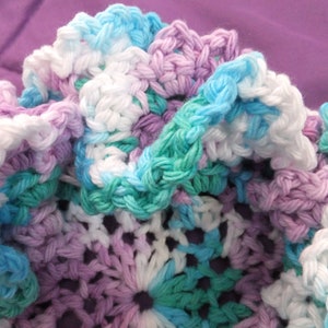 May include: A crocheted fabric with a variety of colors, including white, light blue, teal, and purple. The fabric is made with a variety of stitches and has a textured appearance.