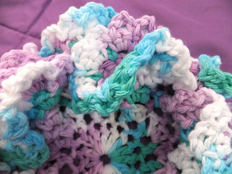 May include: A crocheted fabric with a variety of colors, including white, light blue, teal, and purple. The fabric is made with a variety of stitches and has a textured appearance.