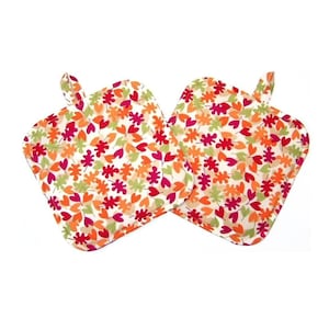 May include: Two square fabric pot holders featuring a repeating pattern of small autumn leaves in shades of red, orange, yellow, and light green. Each pot holder has a small fabric loop attached to the top corner for hanging purposes.