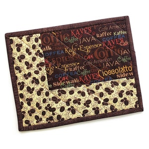 May include: A rectangular coffee-themed quilted coaster. The coaster features a brown border and a patchwork design with coffee bean and text patterns. The text includes words like "coffee," "espresso," and "java."