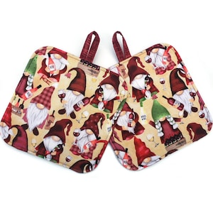 May include: Two beige oven mitts with a repeating pattern of wine-loving gnomes in burgundy hats and coats, holding wine bottles and glasses. The mitts have burgundy hanging loops.
