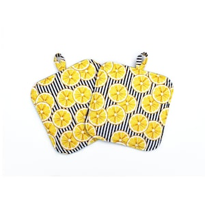 May include: Two square oven mitts with a lemon slice pattern on a black and white striped background. Each mitt has a small loop for hanging. The mitts are yellow, black, and white.