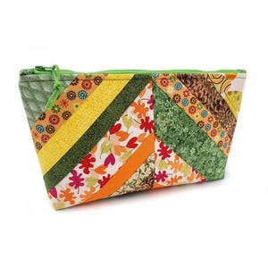 May include: A zippered pouch featuring a quilted light green side panel and a patchwork body composed of diagonal fabric strips. The patterns include autumn leaves, small flowers, green foliage, and brown textures in shades of orange, yellow, and green.