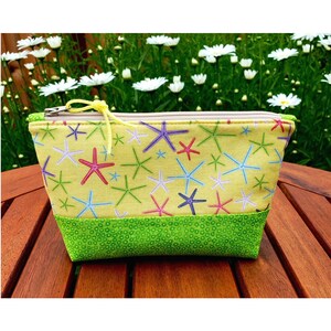 May include: A small, rectangular cosmetic bag with a yellow background and a pattern of colorful starfish. The bottom of the bag is green with a dotted pattern, and it has a zipper closure with a yellow pull.