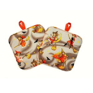 May include: Two square fabric pot holders featuring a vintage-style Halloween print on a light gray background. The pattern displays illustrations of witches in orange dresses, black cats, jack-o'-lanterns, bats, and yellow stars. Each has an orange loop.