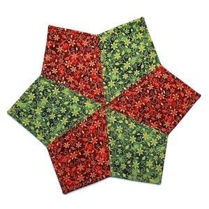 May include: A star-shaped quilted trivet with a festive design. The trivet is made of fabric with a repeating pattern of red and green floral elements. The trivet is designed to protect surfaces from hot dishes and adds a touch of holiday cheer to any kitchen.