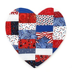 May include: Heart-shaped quilted item with a patchwork design in red, white, and blue. The design incorporates stars, stripes, paisley, and an American flag pattern. The item is likely a decorative piece or a coaster.