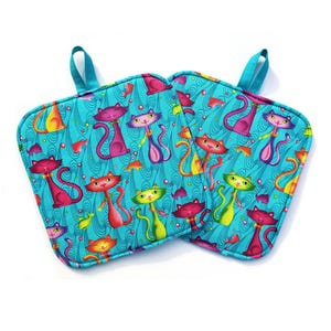 May include: Two square turquoise pot holders with a colorful cat pattern. The cats are in various colors, including red, pink, and yellow, with a turquoise background and small fish. Each pot holder has a turquoise loop for hanging.