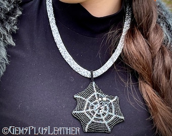 Tooled leather necklace imitating a hammered silver metal with a pendant featuring a pearl spider sitting on a bead embroidered spider web